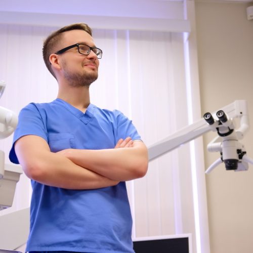 Portrait of a handsome dentist wearing doctor uniform, standing in a dentist clinic.